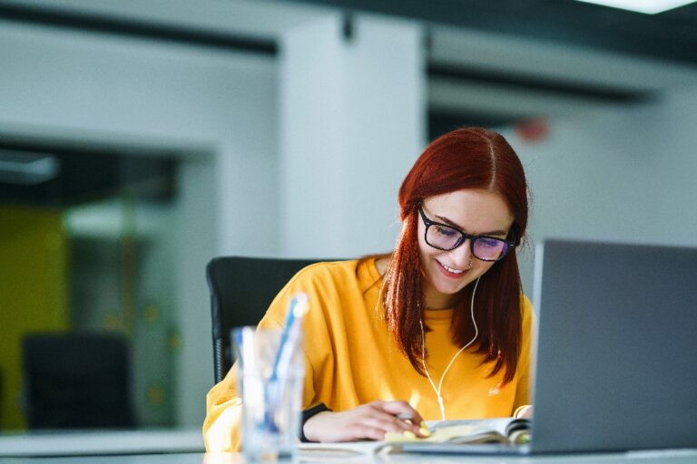 Stock photo of a smiling woman sitting at an office desk looking down at a notebook.