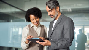 Two busy happy diverse professional business team people working in office with digital tablet. Male executive manager talking to female partners having conversation standing at work using tab.