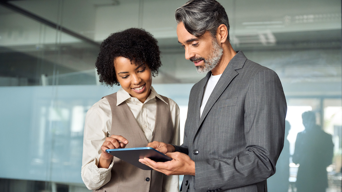 Two busy happy diverse professional business team people working in office with digital tablet. Male executive manager talking to female partners having conversation standing at work using tab.